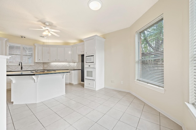 kitchen featuring white cabinetry, backsplash, white appliances, and light tile patterned floors