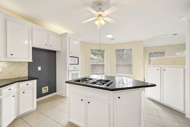 kitchen with light tile patterned floors, white appliances, ceiling fan, white cabinets, and a kitchen island