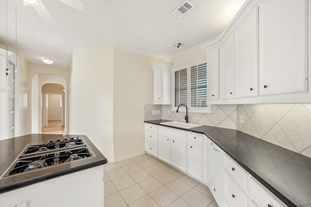 kitchen featuring stainless steel gas cooktop, sink, white cabinetry, light tile patterned floors, and backsplash