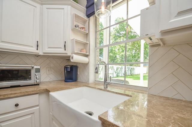 kitchen featuring sink, light stone counters, white cabinets, and backsplash