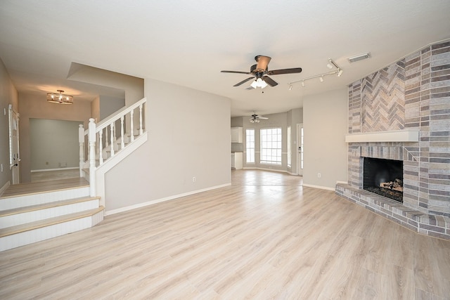 unfurnished living room with baseboards, visible vents, wood finished floors, stairs, and a fireplace