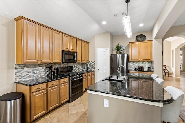 kitchen featuring sink, hanging light fixtures, dark stone countertops, an island with sink, and black appliances