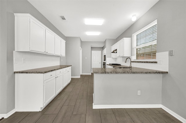 kitchen with sink, white cabinetry, tasteful backsplash, kitchen peninsula, and dark stone counters