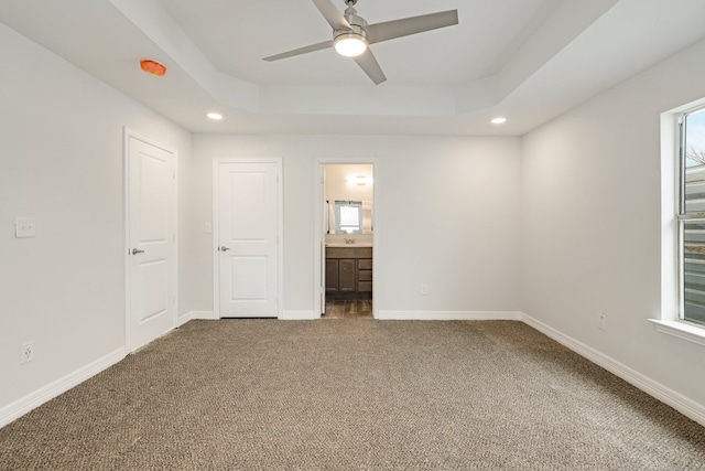 unfurnished bedroom with a raised ceiling, carpet flooring, connected bathroom, and multiple windows