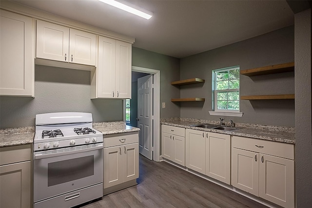 kitchen featuring white cabinetry, sink, light stone counters, and white gas range oven