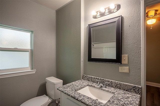 half bath featuring a textured wall, vanity, and toilet