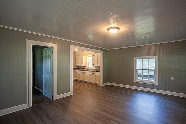 empty room featuring crown molding, dark wood finished floors, and baseboards