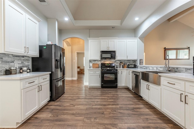 kitchen with white cabinetry, dark wood-type flooring, decorative backsplash, and black appliances