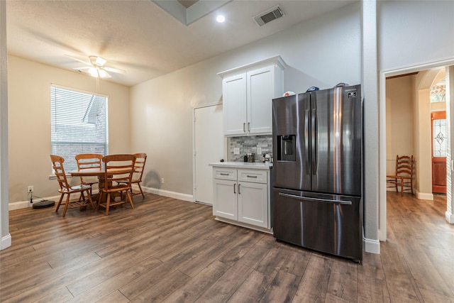 kitchen with dark wood-type flooring, stainless steel fridge, ceiling fan, white cabinetry, and decorative backsplash