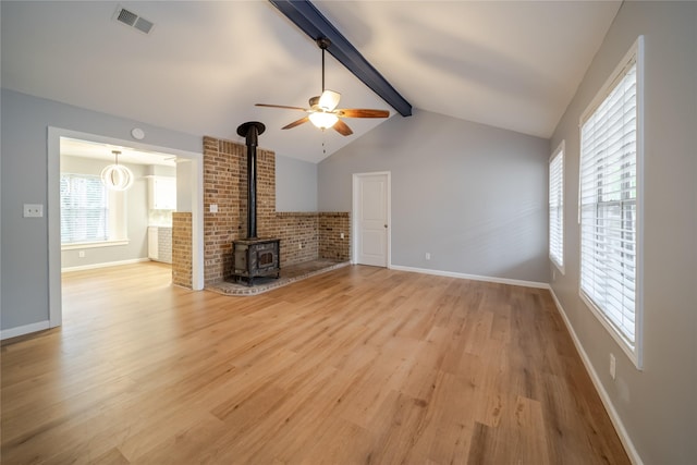 unfurnished living room featuring lofted ceiling with beams, ceiling fan, a wood stove, and light hardwood / wood-style floors