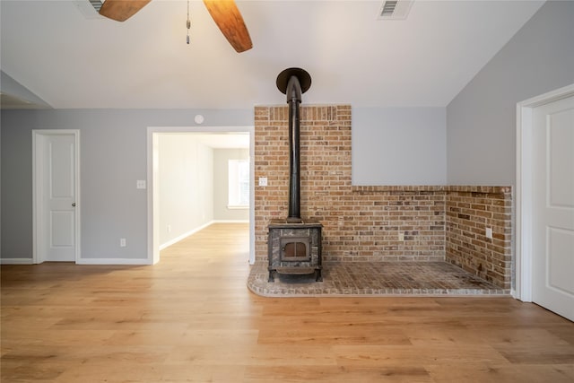 unfurnished living room featuring ceiling fan, light wood-type flooring, vaulted ceiling, and a wood stove