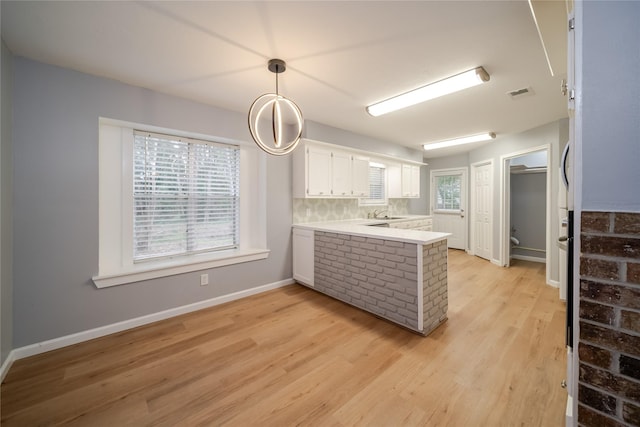 kitchen featuring pendant lighting, light hardwood / wood-style flooring, white cabinetry, backsplash, and kitchen peninsula