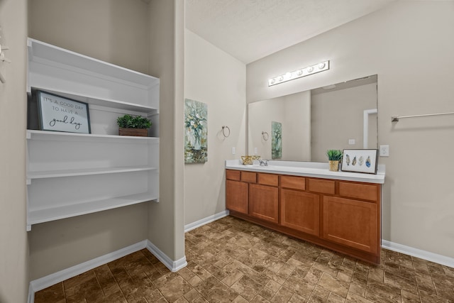 bathroom featuring stone finish floor, vanity, and baseboards