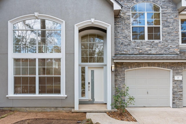 entrance to property with an attached garage, stone siding, and stucco siding