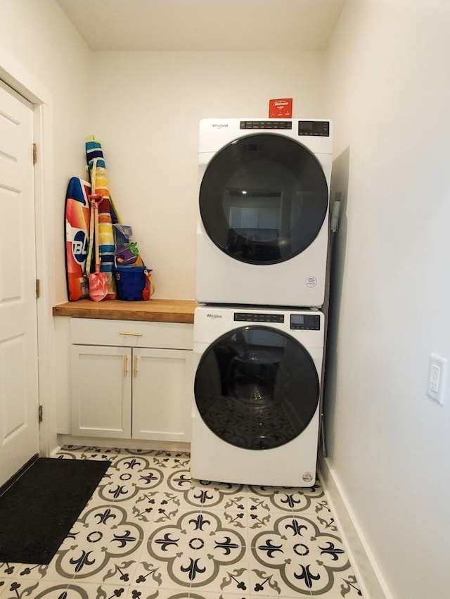 clothes washing area with cabinets, stacked washer and clothes dryer, and light tile patterned flooring