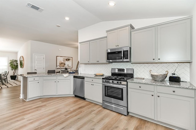 kitchen featuring lofted ceiling, sink, light stone counters, kitchen peninsula, and stainless steel appliances