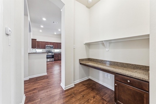 kitchen featuring sink, appliances with stainless steel finishes, dark hardwood / wood-style floors, built in desk, and dark stone counters