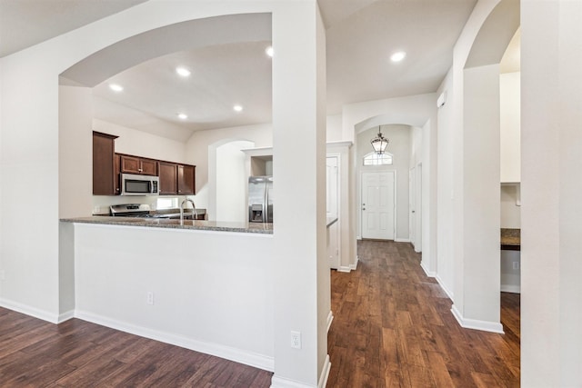 kitchen with appliances with stainless steel finishes, stone counters, dark hardwood / wood-style floors, dark brown cabinetry, and kitchen peninsula