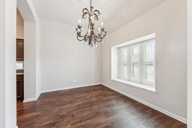 spare room with dark wood-type flooring and an inviting chandelier