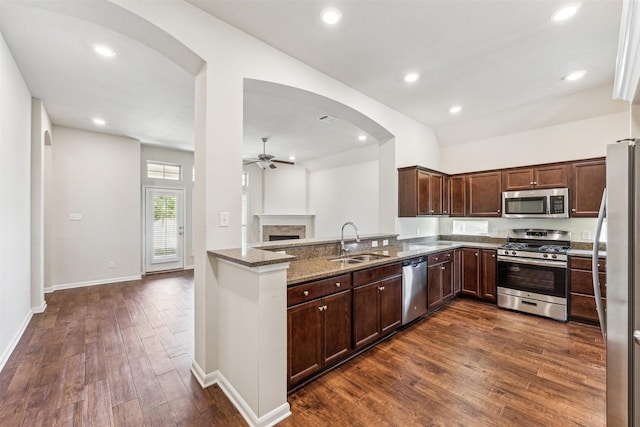 kitchen featuring sink, dark hardwood / wood-style flooring, dark stone counters, kitchen peninsula, and stainless steel appliances