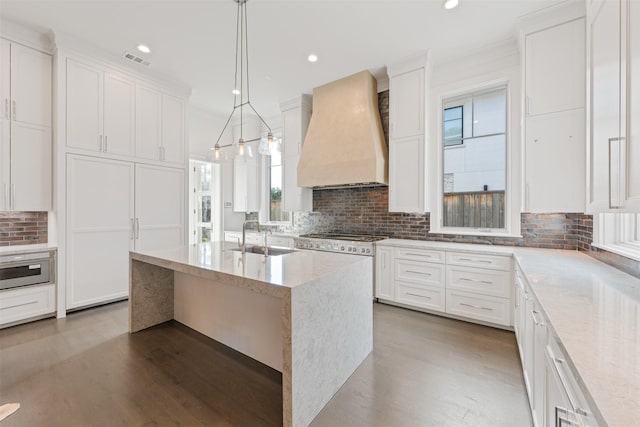 kitchen with pendant lighting, an island with sink, sink, white cabinets, and custom exhaust hood