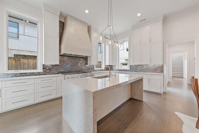 kitchen with an island with sink, sink, white cabinets, custom exhaust hood, and stainless steel gas cooktop