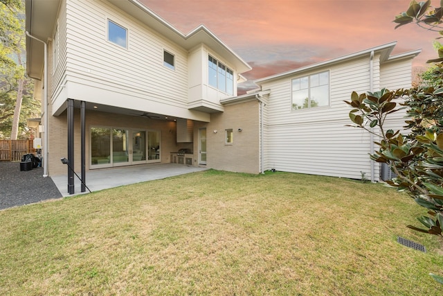 back house at dusk with a patio, a balcony, and a lawn