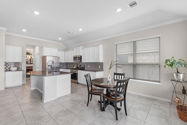 kitchen featuring a center island with sink, dark stone countertops, ornamental molding, appliances with stainless steel finishes, and white cabinets