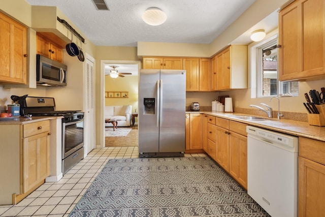 kitchen with light tile patterned flooring, appliances with stainless steel finishes, sink, ceiling fan, and a textured ceiling