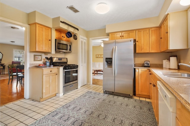 kitchen with sink, stainless steel appliances, a textured ceiling, light tile patterned flooring, and light brown cabinetry