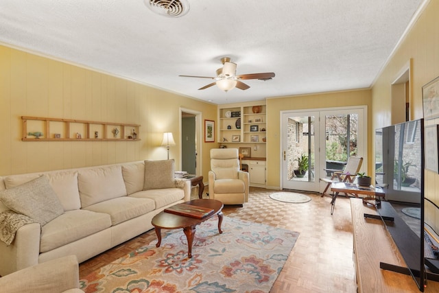 living room featuring built in shelves, ceiling fan, crown molding, and a textured ceiling