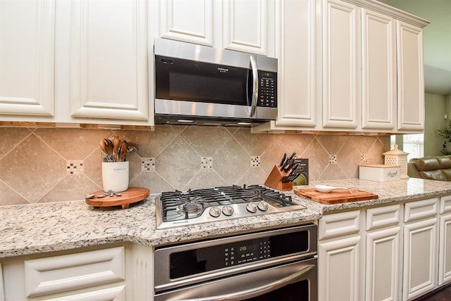 kitchen with white cabinetry, decorative backsplash, light stone countertops, and appliances with stainless steel finishes