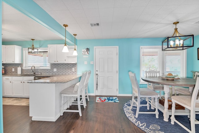 kitchen with hanging light fixtures, a kitchen breakfast bar, kitchen peninsula, light stone countertops, and white cabinets