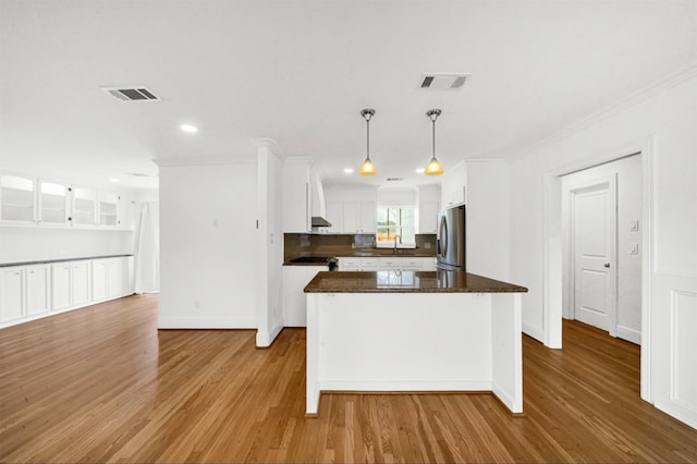 kitchen featuring stainless steel refrigerator, white cabinets, a kitchen island, decorative light fixtures, and light wood-type flooring