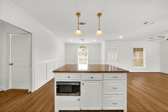 kitchen with wood-type flooring, a kitchen island, pendant lighting, and white cabinets