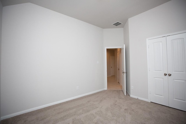 unfurnished bedroom featuring vaulted ceiling, light colored carpet, and a closet