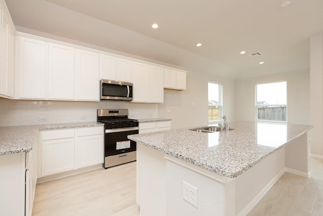 kitchen with sink, white cabinetry, light stone counters, appliances with stainless steel finishes, and an island with sink