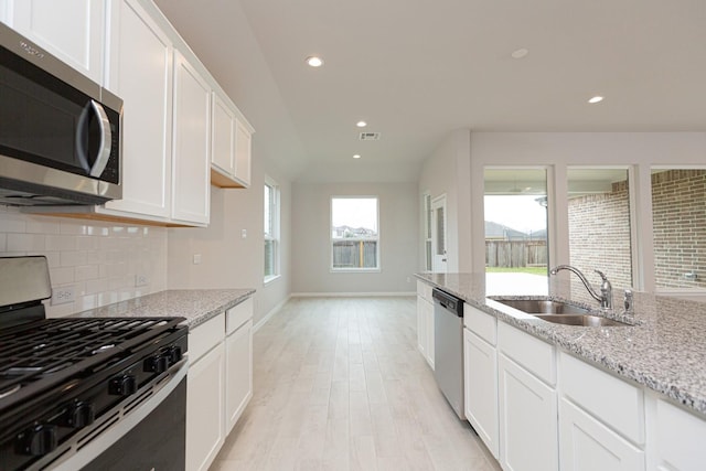 kitchen with appliances with stainless steel finishes, tasteful backsplash, white cabinetry, sink, and light stone countertops