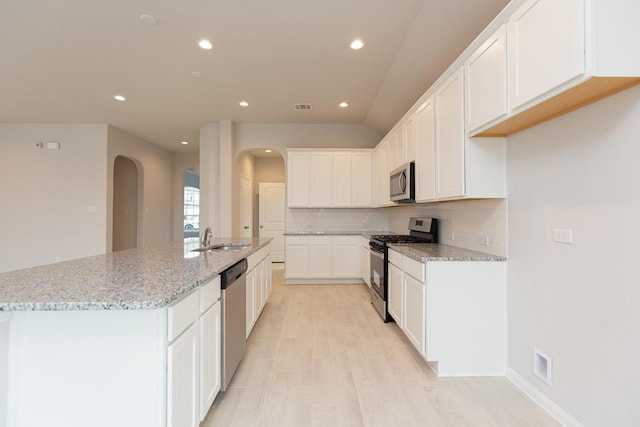 kitchen featuring sink, a kitchen island with sink, stainless steel appliances, light stone countertops, and white cabinets