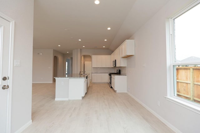 kitchen featuring appliances with stainless steel finishes, white cabinetry, an island with sink, light stone counters, and light hardwood / wood-style floors