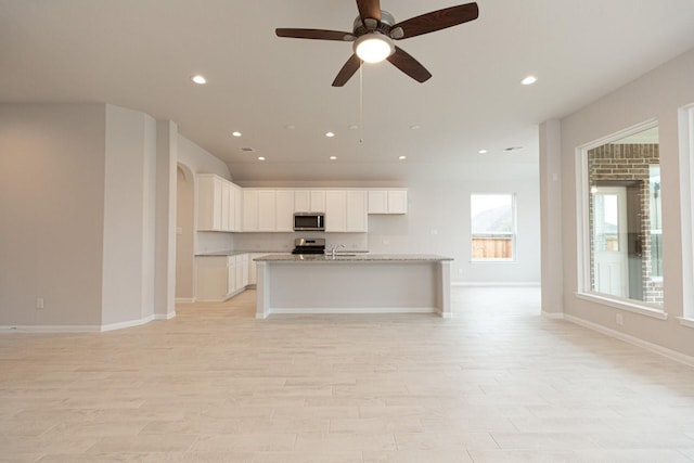 kitchen with sink, light stone counters, a center island with sink, appliances with stainless steel finishes, and white cabinets