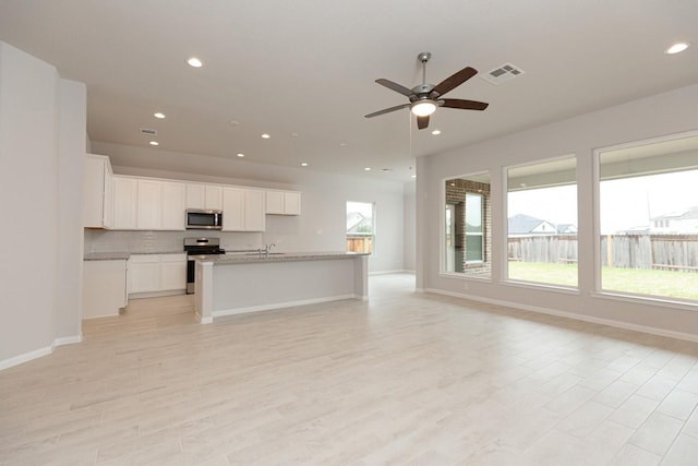 kitchen with sink, light wood-type flooring, stainless steel appliances, a kitchen island with sink, and white cabinets