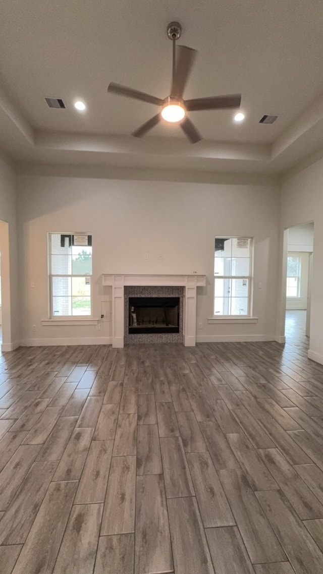 unfurnished living room featuring ceiling fan, plenty of natural light, a raised ceiling, and light hardwood / wood-style floors