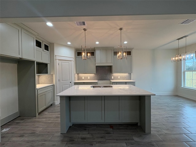 kitchen featuring hanging light fixtures, an inviting chandelier, a center island with sink, and light stone counters