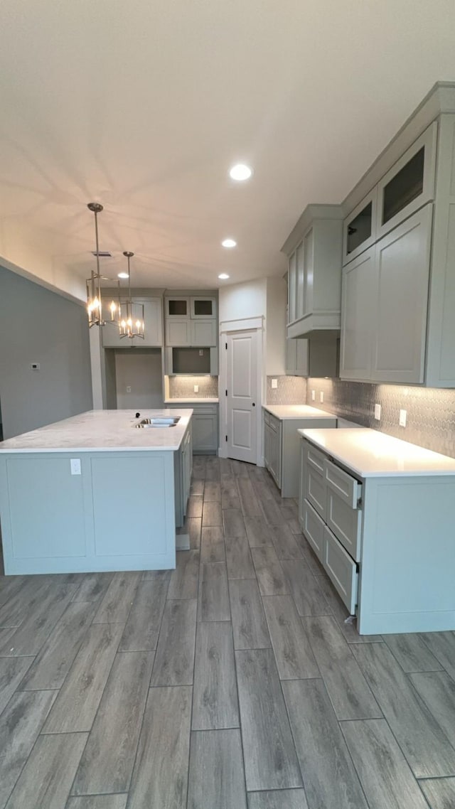 kitchen with gray cabinetry, decorative light fixtures, a kitchen island, a notable chandelier, and backsplash