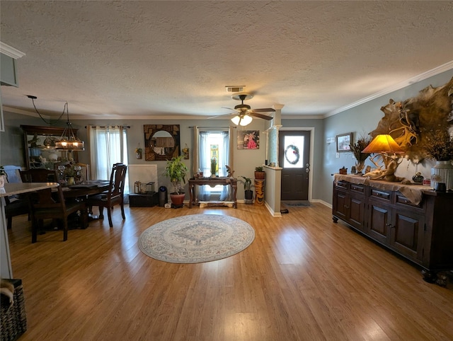 living area with a textured ceiling, wood finished floors, visible vents, and crown molding