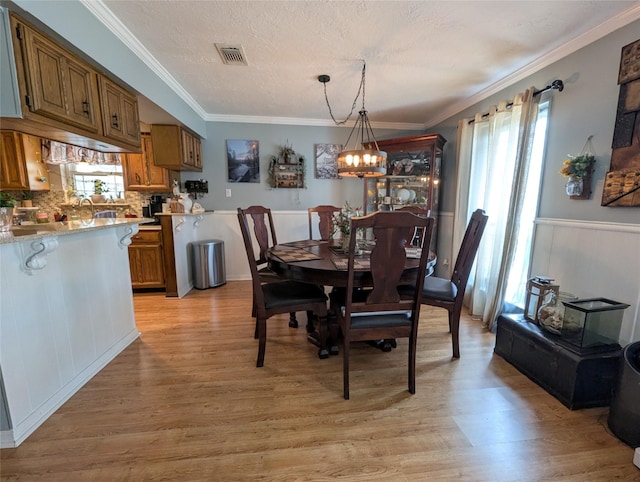 dining area with visible vents, crown molding, a notable chandelier, and light wood finished floors