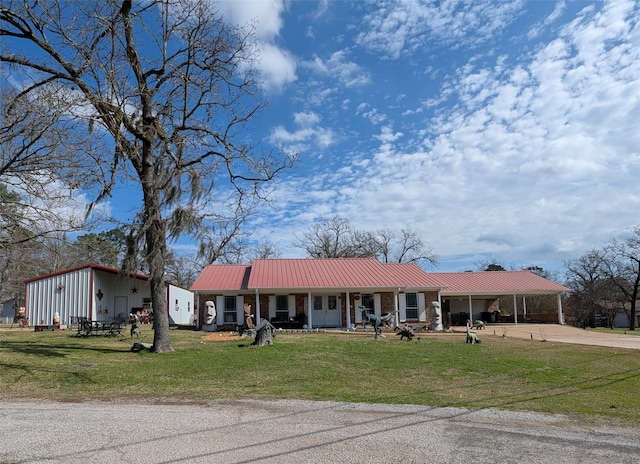 view of front of property with brick siding, a porch, a front yard, metal roof, and driveway