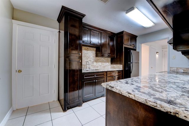 kitchen featuring black fridge, dark brown cabinetry, decorative backsplash, and light tile patterned floors