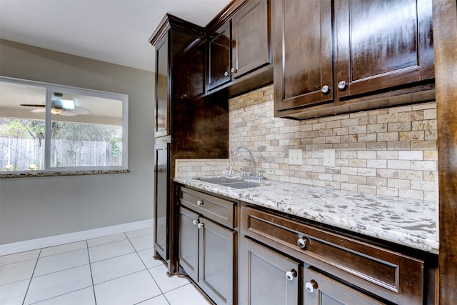 kitchen with light tile patterned flooring, sink, dark brown cabinets, light stone countertops, and decorative backsplash